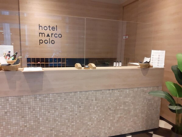 A hotel reception desk with a mosaic tile design, a sign reading "hotel marco polo," and a plant to the right. - Hotel Marco Polo (Münster)