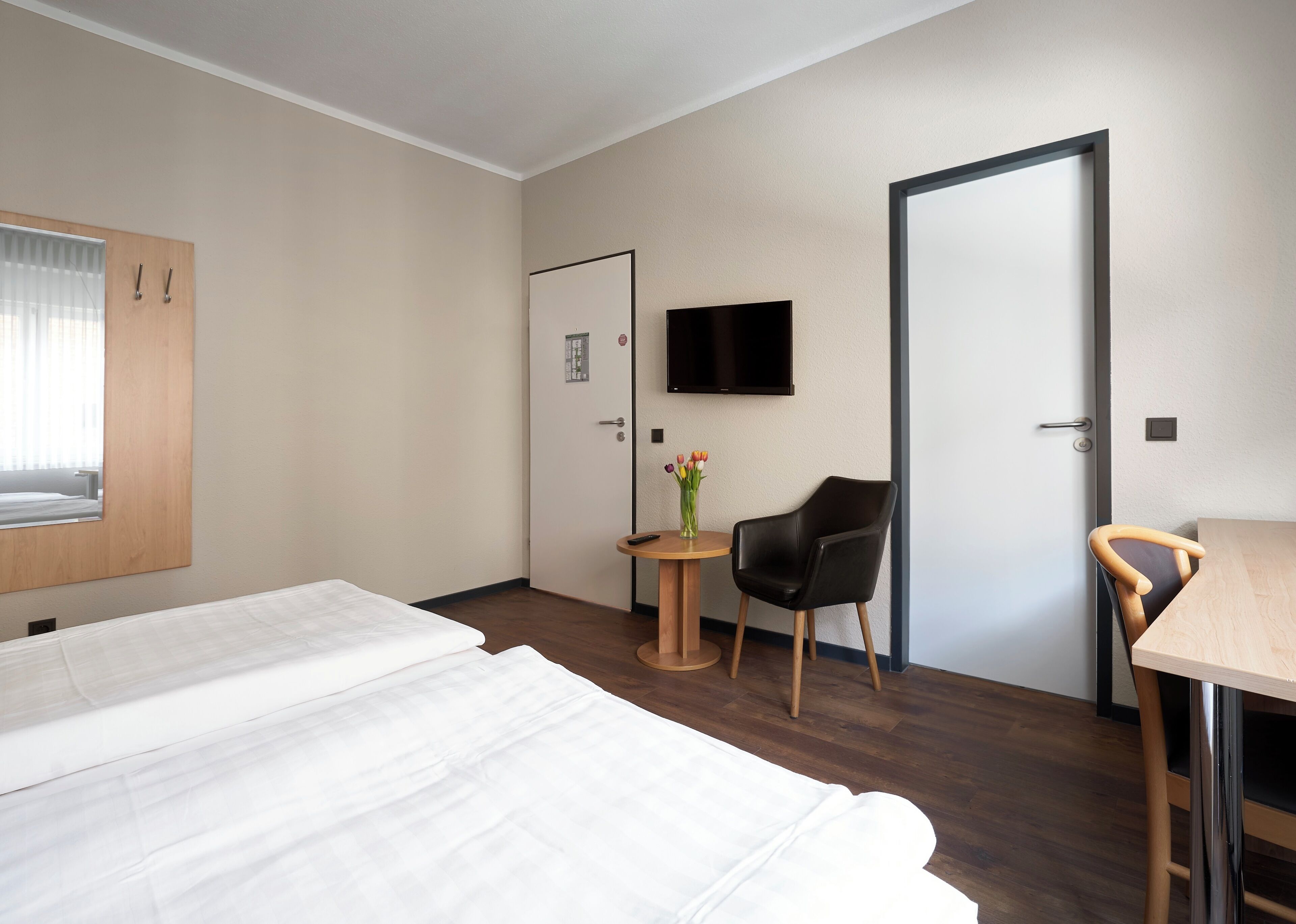 Una camera d'albergo con un letto, una scrivania, una sedia, una televisione e un tavolino con un vaso di fiori.
