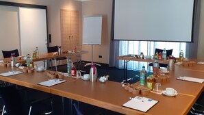 A conference room with long tables, chairs, a whiteboard, and various items like cups, bottles, and notepads. - Hotel Marco Polo (Münster)