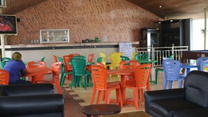 A restaurant with colorful plastic chairs and tables, a wooden ceiling, and a sign advertising games. - Tourist Castle Hotel and Suites (Calabar)
