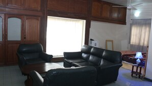 A living room with a sofa, armchair, and coffee table. There is a window with curtains, a ceiling fan, and a lamp on a side table. - Tourist Castle Hotel and Suites (Calabar)
