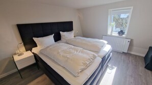 Un lit double avec une literie blanche, une table de chevet, une lampe de chevet, une fenêtre donnant sur un paysage agréable et un radiateur.