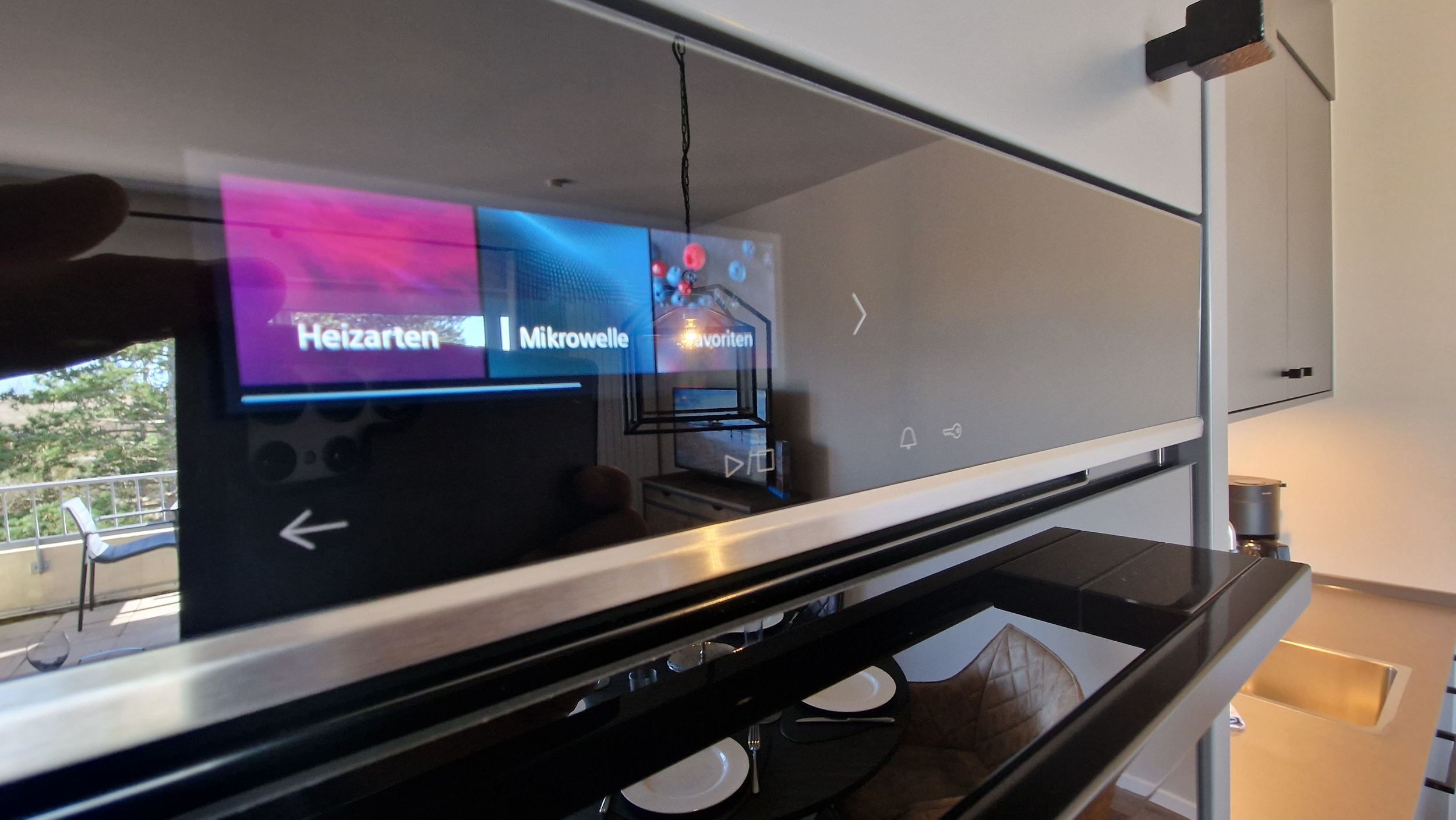 A modern interior with a digital display, a dining area with a table and chairs, and a kitchen area with a sink and stove.