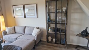 Un salon avec un canapé gris, une vitrine contenant des objets décoratifs et deux tableaux encadrés accrochés au mur.