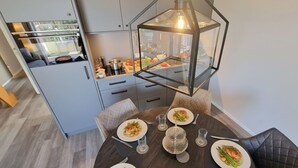 Une cuisine moderne avec un coin repas, comprenant une table ronde sur laquelle sont disposés des plats, un luminaire suspendu à six faces et une vue sur le plan de travail de la cuisine.