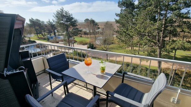 Un balcon avec une table et des chaises, un barbecue et une vue sur un parc et des immeubles.