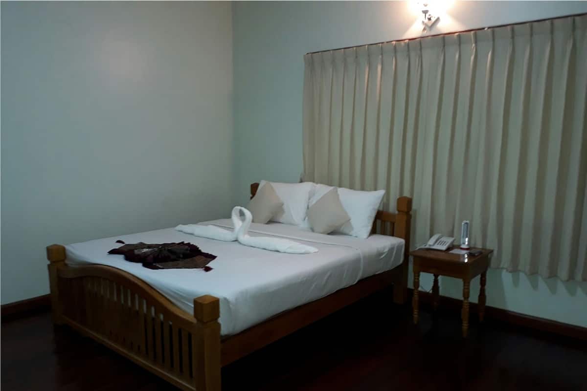 A neatly made bed with a wooden headboard, a bedside table with a lamp, and a curtain on the window.