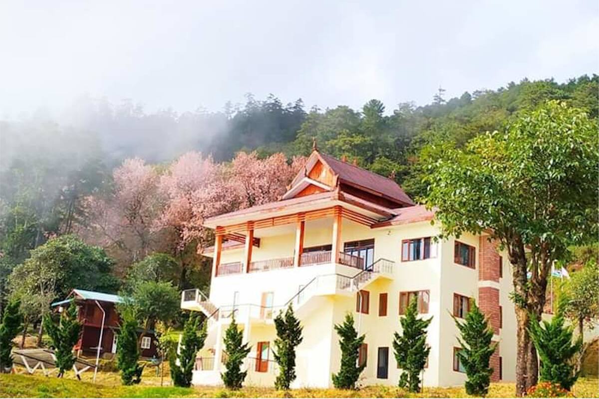 A multi-story building with a balcony on the upper floor, surrounded by trees and greenery.