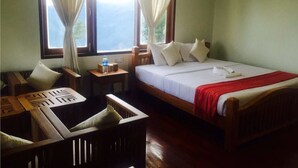 Habitación de hotel con cama, una mesita con una botella, una silla y un ventanal con cortinas.