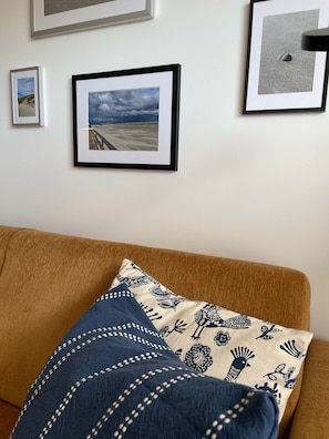Una habitación con un sofá marrón, un cojín estampado y tres cuadros en la pared.