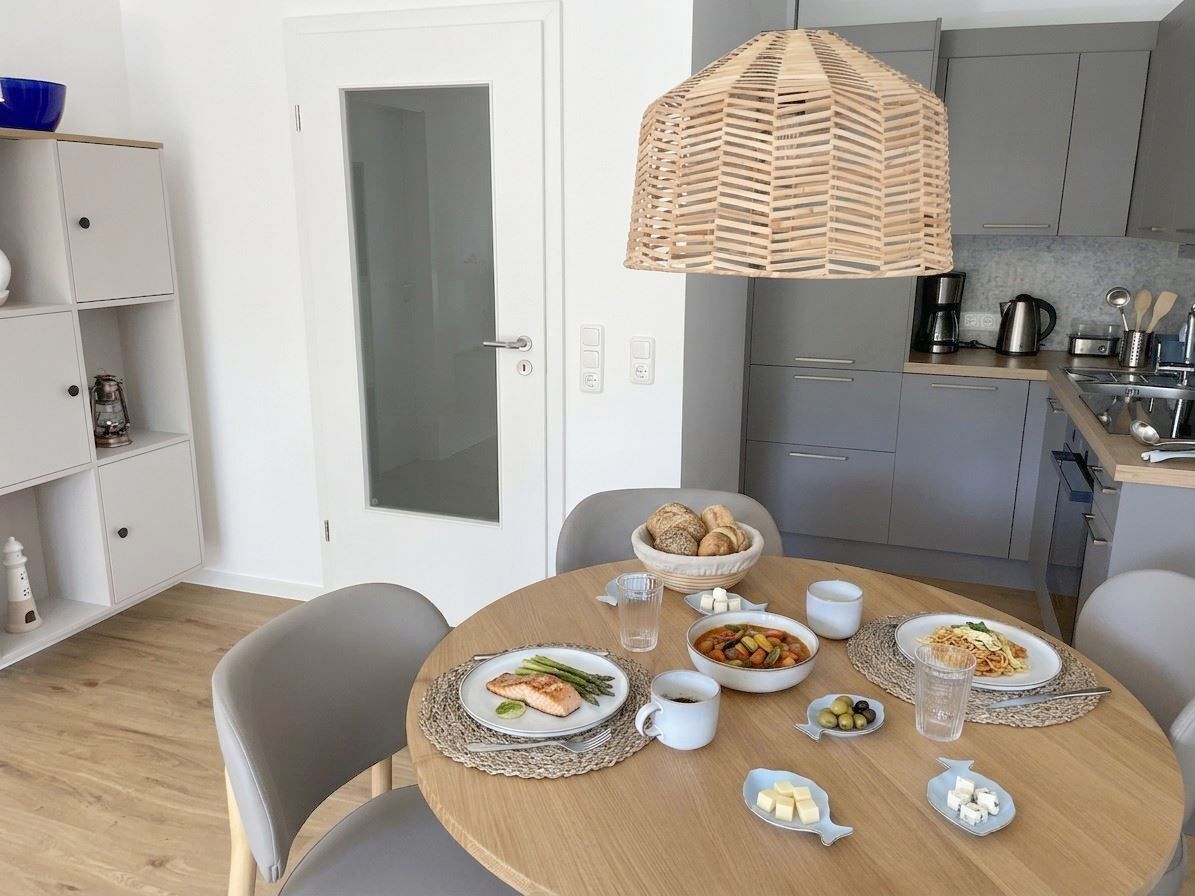 A dining area with a round table set for two, a kitchen in the background, and a white door.