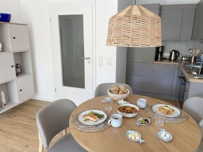 A dining area with a round table set for two, a kitchen in the background, and a white door.