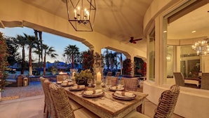 An outdoor dining area with a wooden table set for four, surrounded by wicker chairs. - Escape to Legends - Pool, Games & Amazing Mountain Views in PGA West #067651 5br (La Quinta)