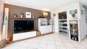 A modern living room with a flat-screen TV, a glass-fronted cabinet, and a fireplace. - House Friesenperle - House Friesenperle Whg 01 (Sankt Peter-Ording)
