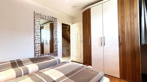 A bedroom with a bed, a wardrobe, a mirror, and a staircase leading to another room.