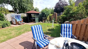 A backyard with two striped chairs, a table, and a grill.