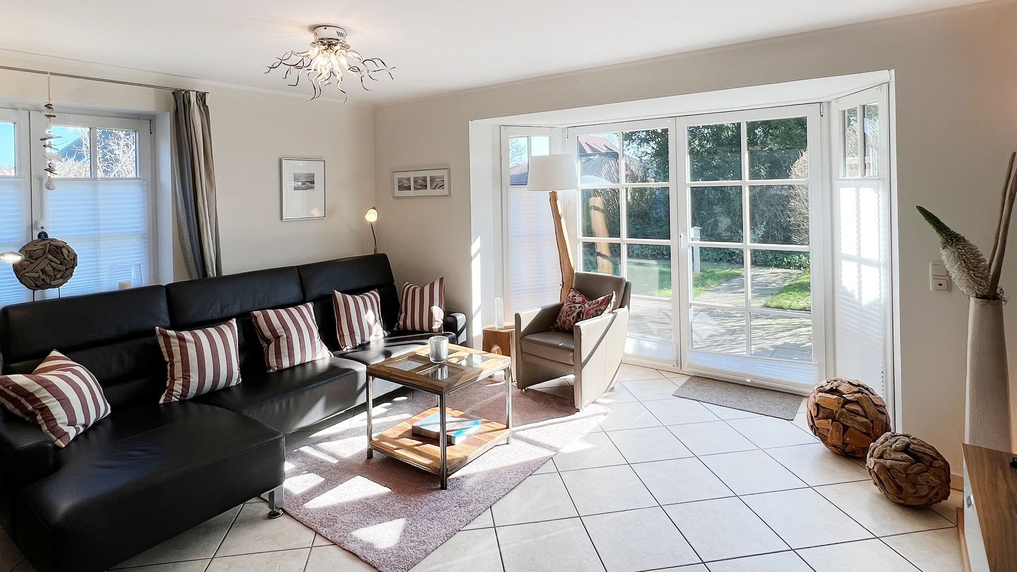 A modern living room with a black sofa, a glass coffee table, and a chair. There is a large window with a view of greenery outside.