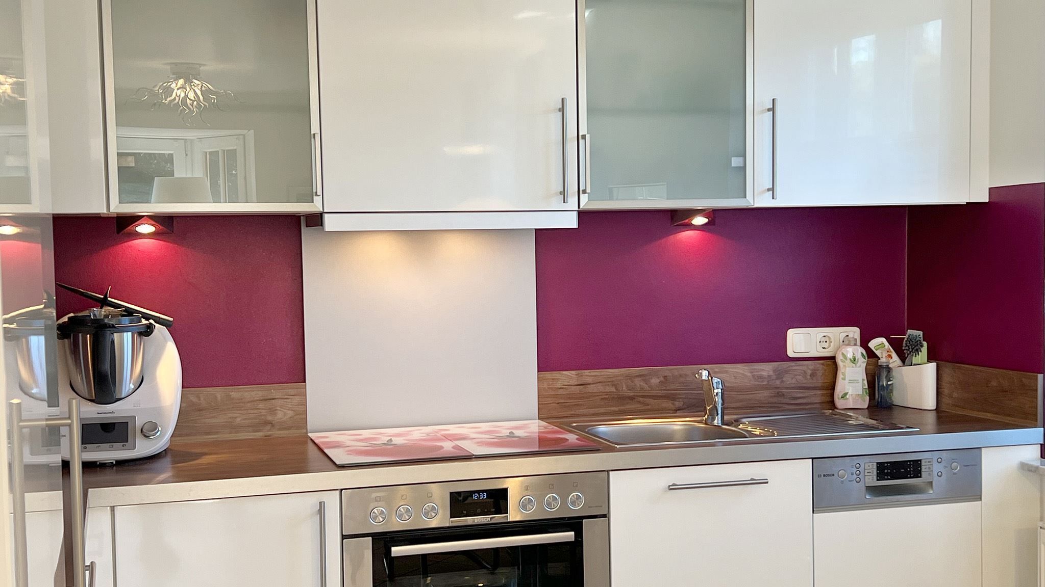 A modern kitchen with white cabinets, a stainless steel sink, a Bosch oven, and a built-in induction cooktop.