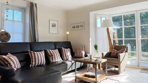 A modern living room with a black sofa, striped pillows, a wooden coffee table, and a chair with a patterned cushion. - House Friesenperle - House Friesenperle Whg 01 (Sankt Peter-Ording)