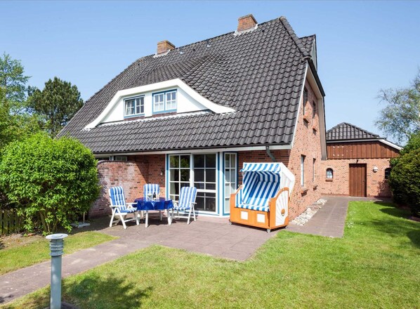A two-story house with a tiled roof, a brick exterior, and a covered patio area with outdoor furniture.