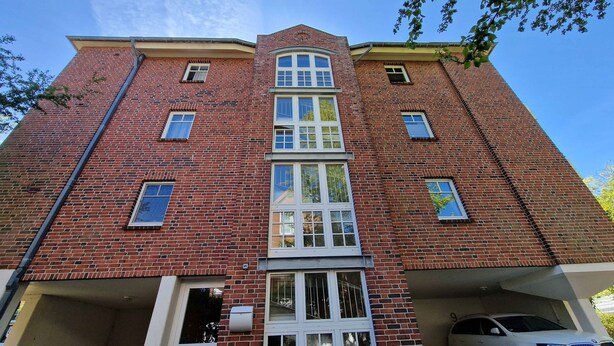 A multi-story brick building with a central staircase, multiple windows, and a parking garage. - 035-02 (Room category) - House Calidris (Sankt Peter-Ording)
