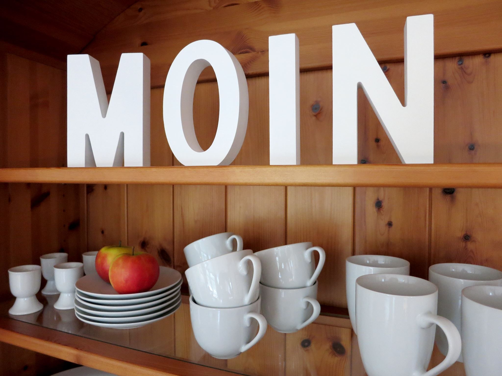A wooden shelf with white mugs and plates, and a red apple.