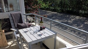 A balcony with a table, two chairs, a bottle of wine, and a glass of wine. - 035-02 (Room category) - House Calidris (Sankt Peter-Ording)
