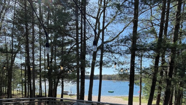 En terrass med en soffa och ett soffbord, med utsikt över en sjö, träd och en strand i bakgrunden.