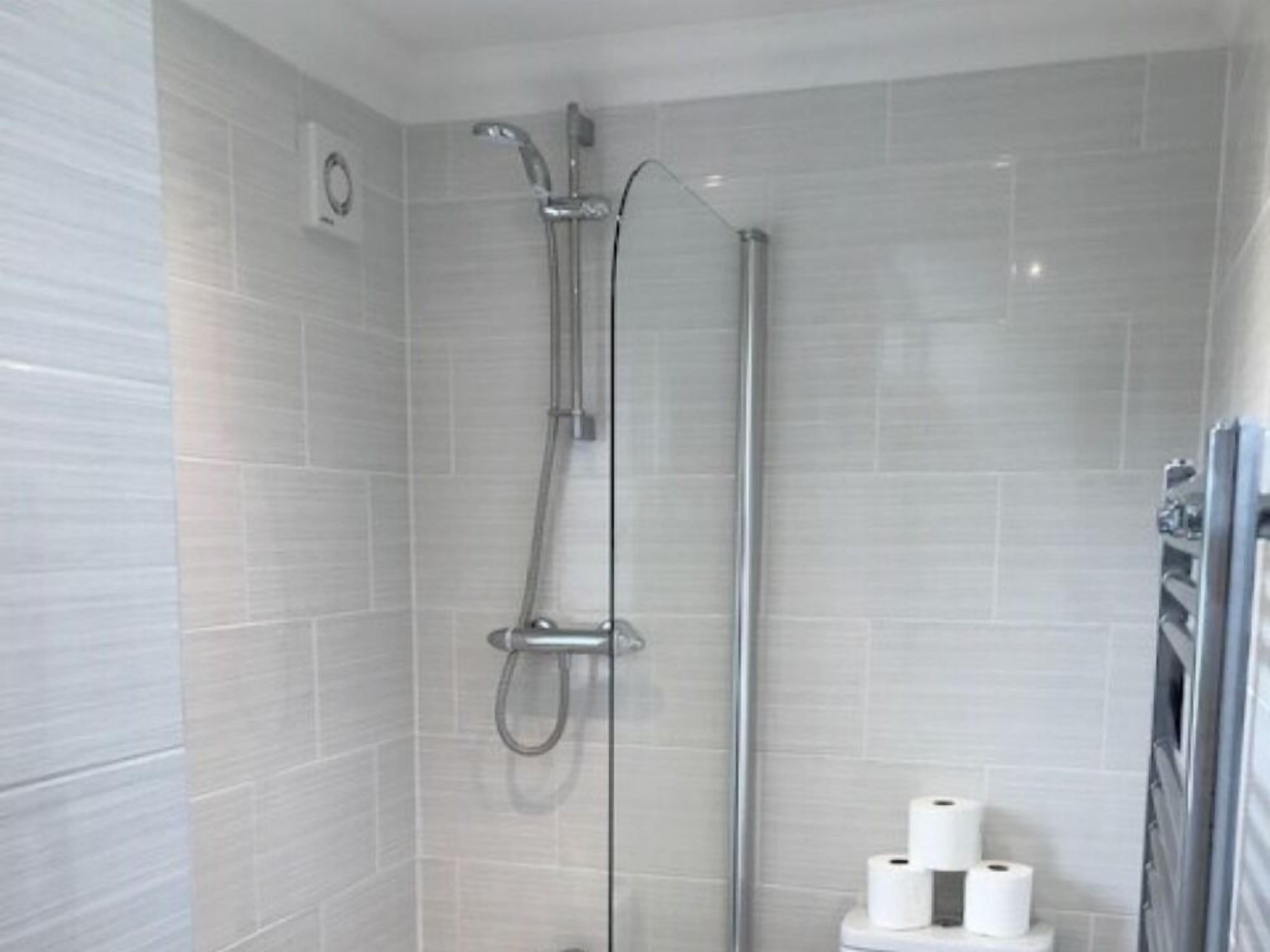 A shower with a glass door, a towel rack, and a toilet with toilet paper.