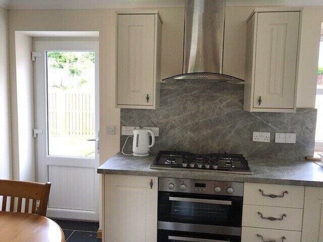 A compact kitchen with a gas stove, oven, and a built-in range hood. There is a white countertop and a wooden chair.