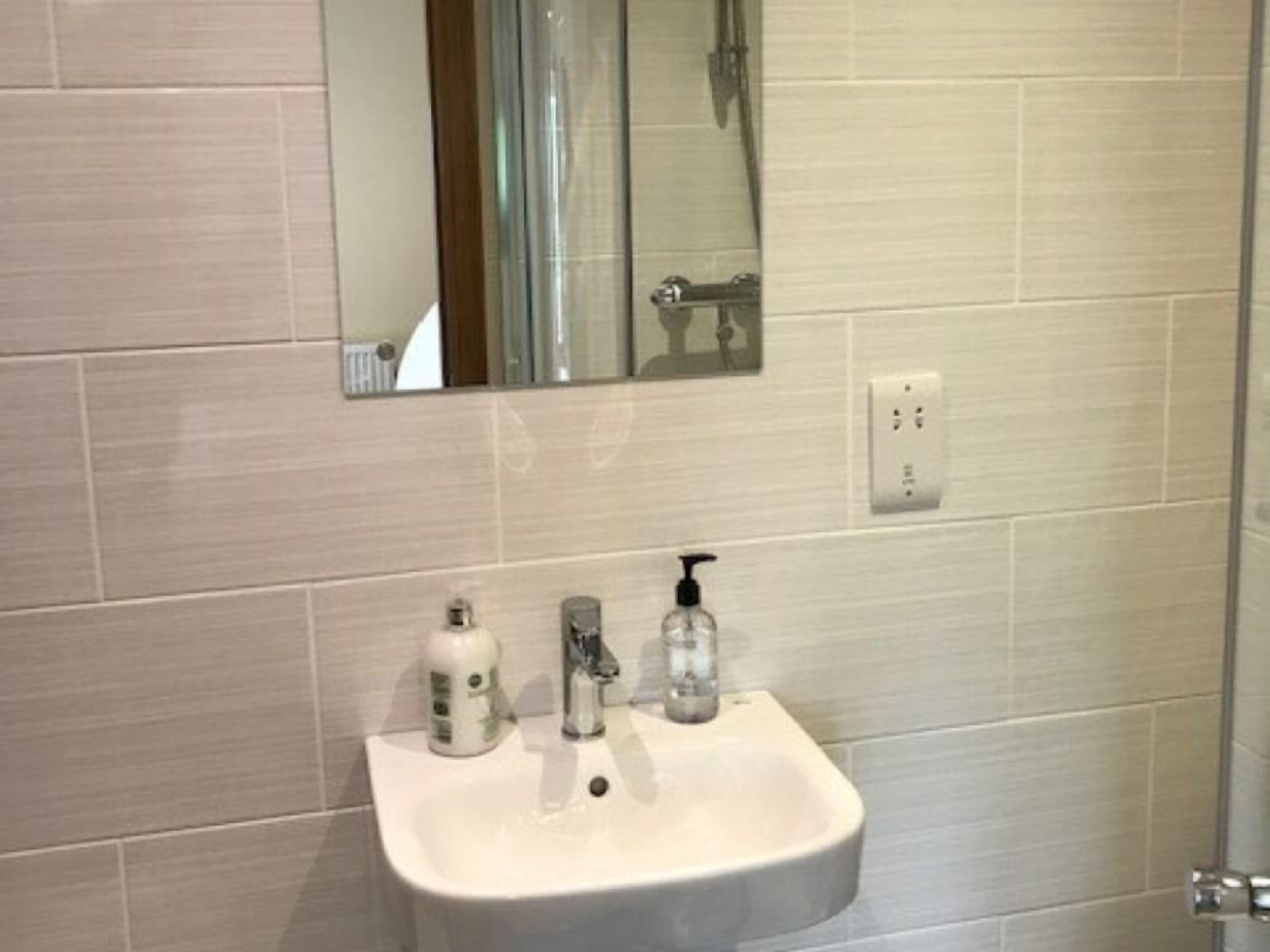 A bathroom with a white sink, two soap dispensers, a mirror, and a shower area.