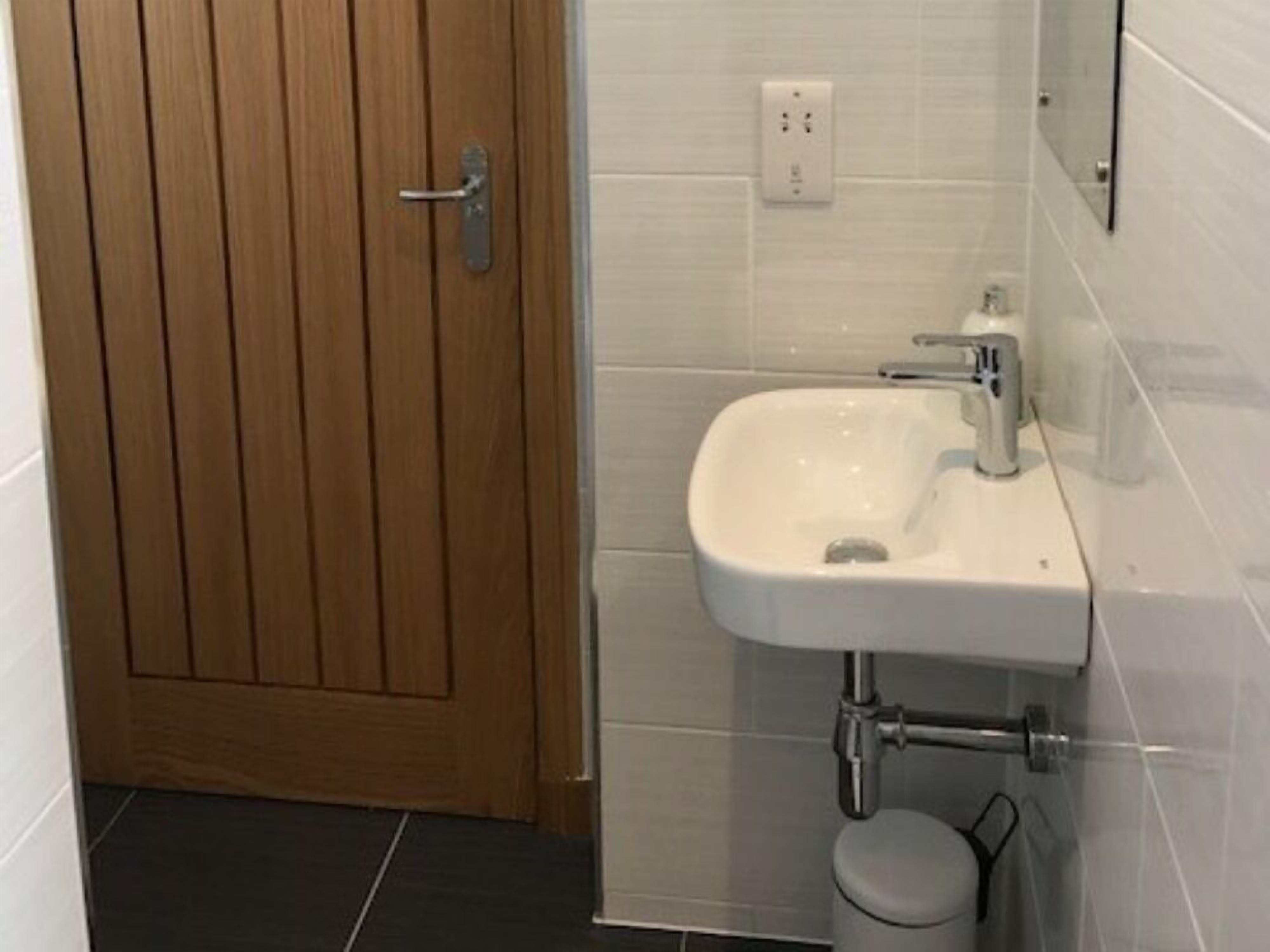 Une salle de bain avec une porte en bois, un lavabo blanc et des murs carrelés.