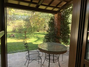 An outdoor patio with a glass table and metal chairs, overlooking a well-maintained garden with various plants and a lawn. - Antica Pietrara (Formello)