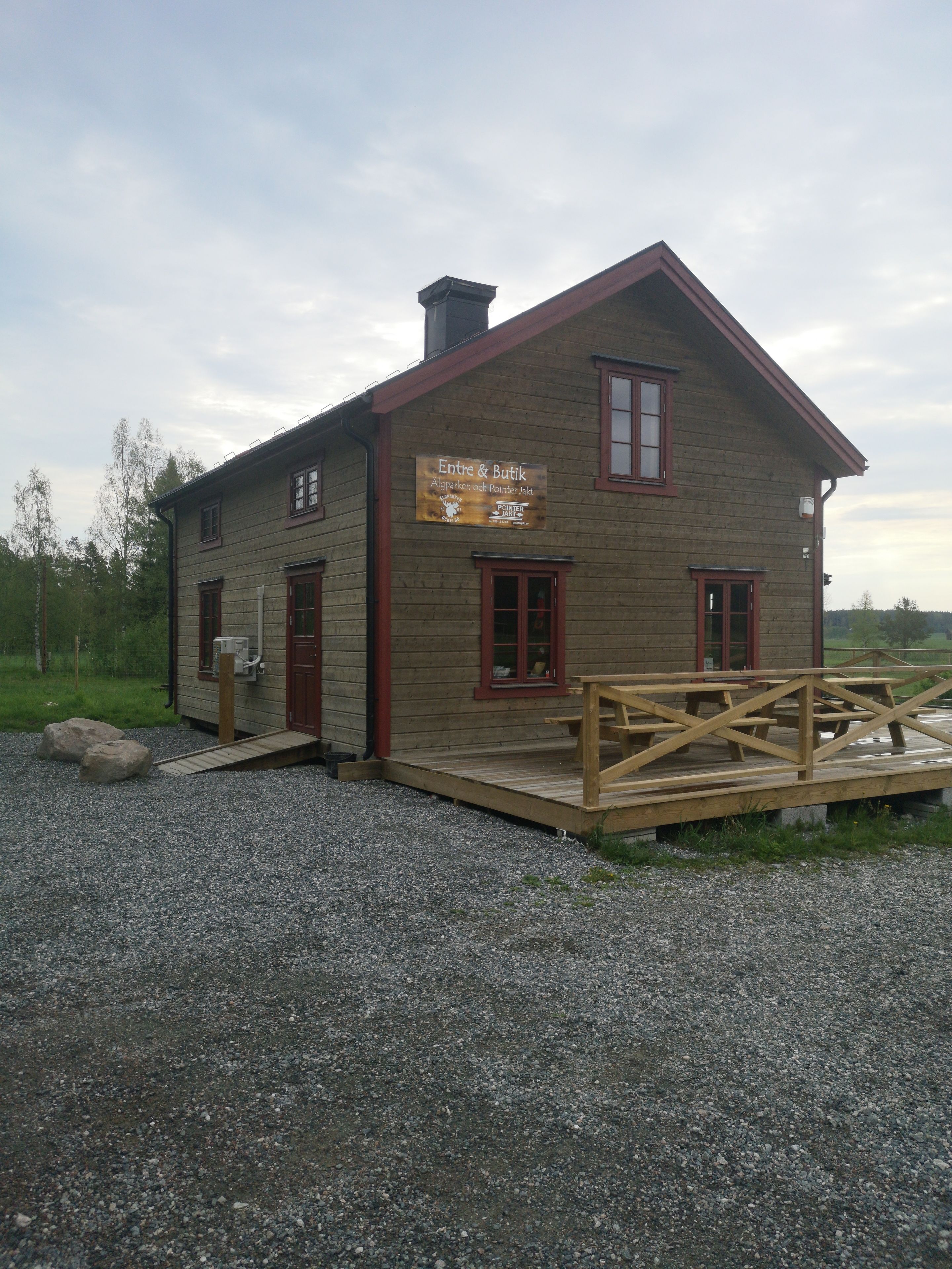 A wooden building with a signboard, a wooden deck, and a gravel driveway.