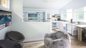 Una cocina moderna con armarios blancos, un comedor y vistas a la playa a través de una ventana.
