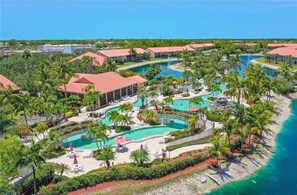 Relax by the resort's multiple pools surrounded by lush greenery and palm trees, adjacent to a beach.