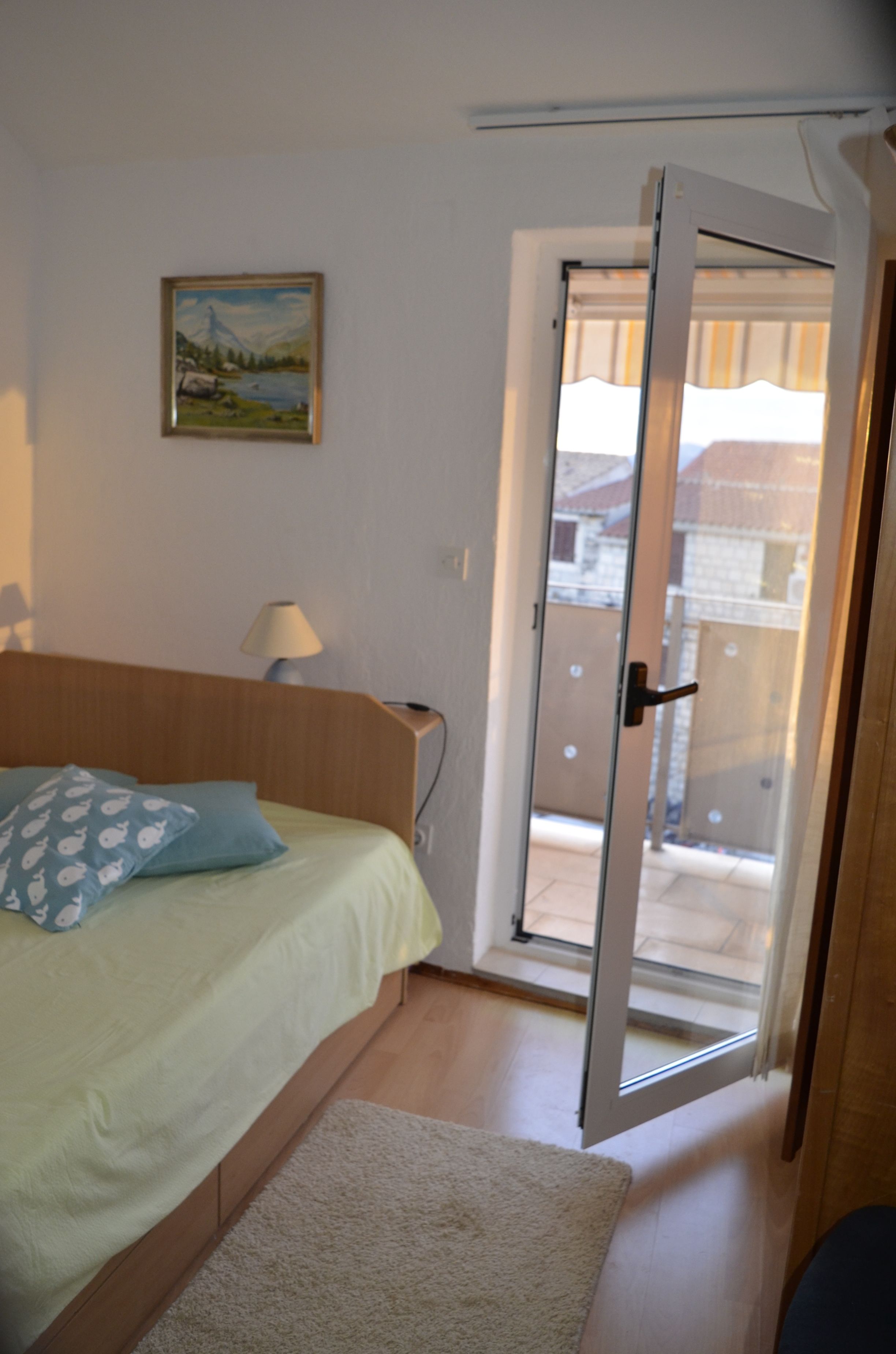 A bedroom with a bed, a painting on the wall, a lamp, and a sliding glass door leading to an outdoor area.
