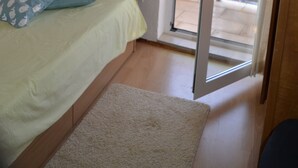 A bedroom with a bed, a painting on the wall, a lamp, and a sliding glass door leading to an outdoor area. - Apartments Kastilac (Kastela)