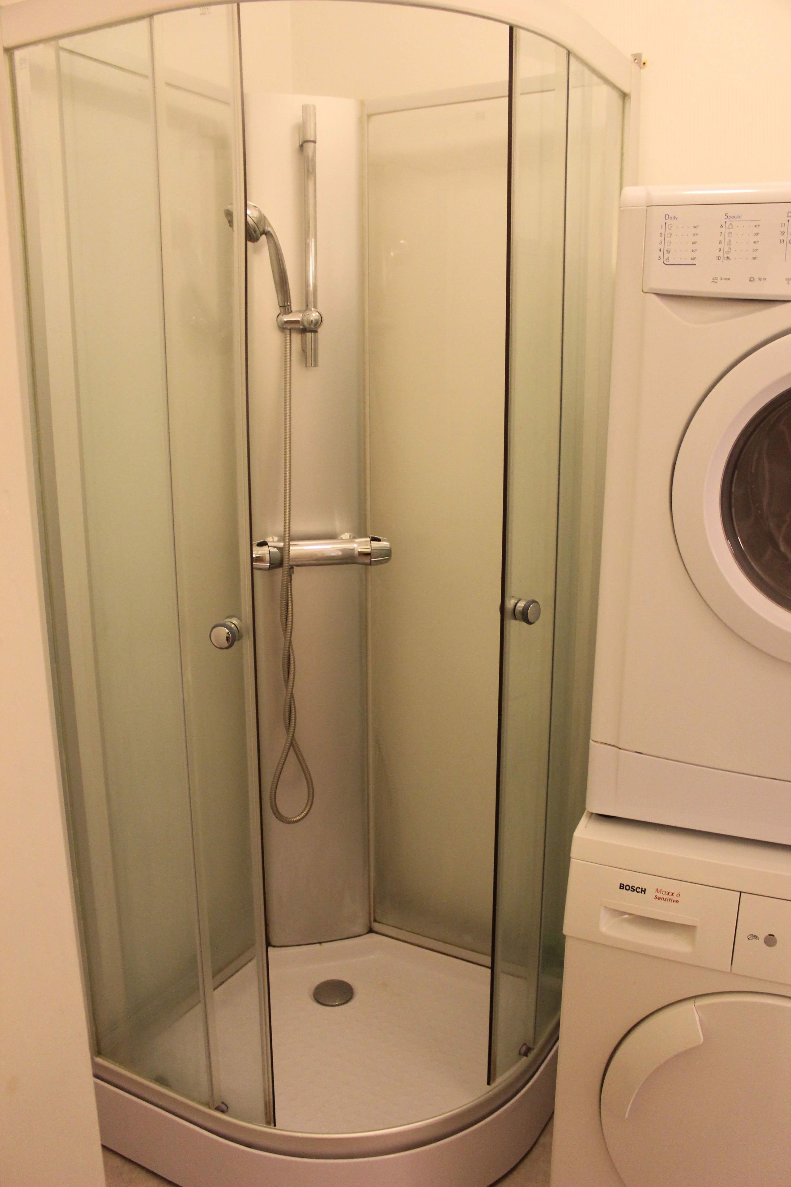 A corner shower enclosure with a glass door and a built-in washing machine.