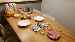 Une table de salle à manger en bois, mise pour le petit-déjeuner, avec du pain, du beurre, du fromage et une tranche de jambon.