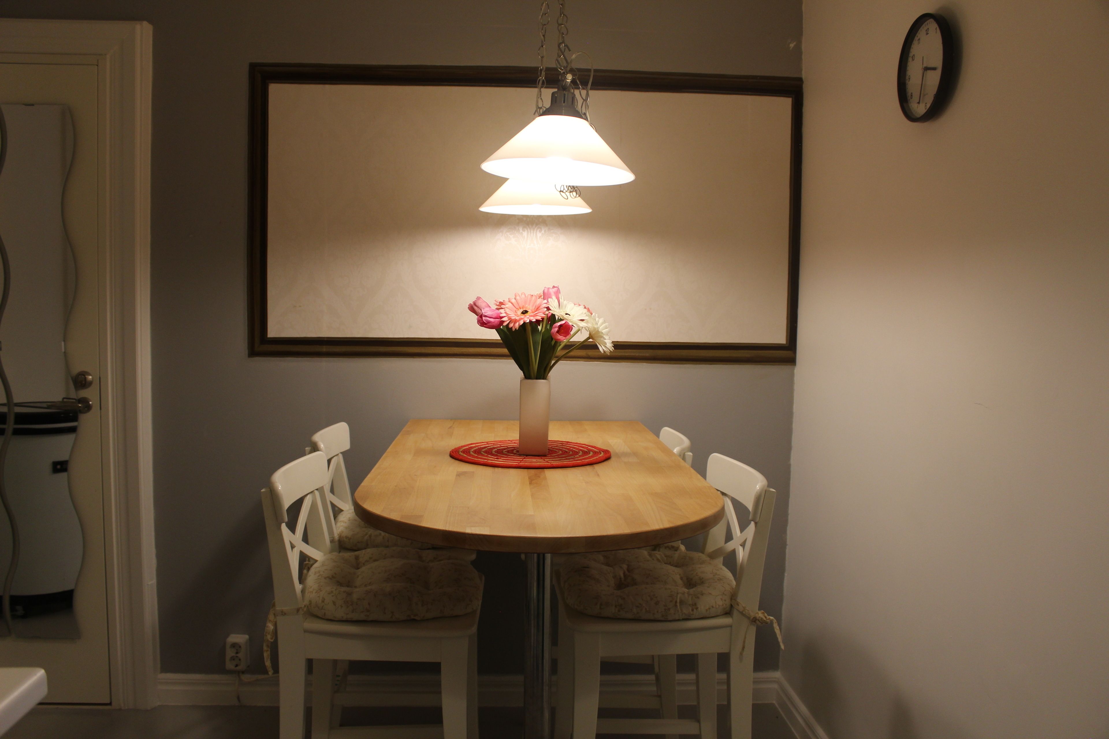 A dining area with a wooden table, white chairs, a vase with flowers, and a hanging lamp.