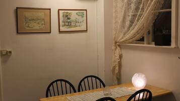 A dining area with a wooden table, four chairs, a vase, and two framed artworks on the wall.