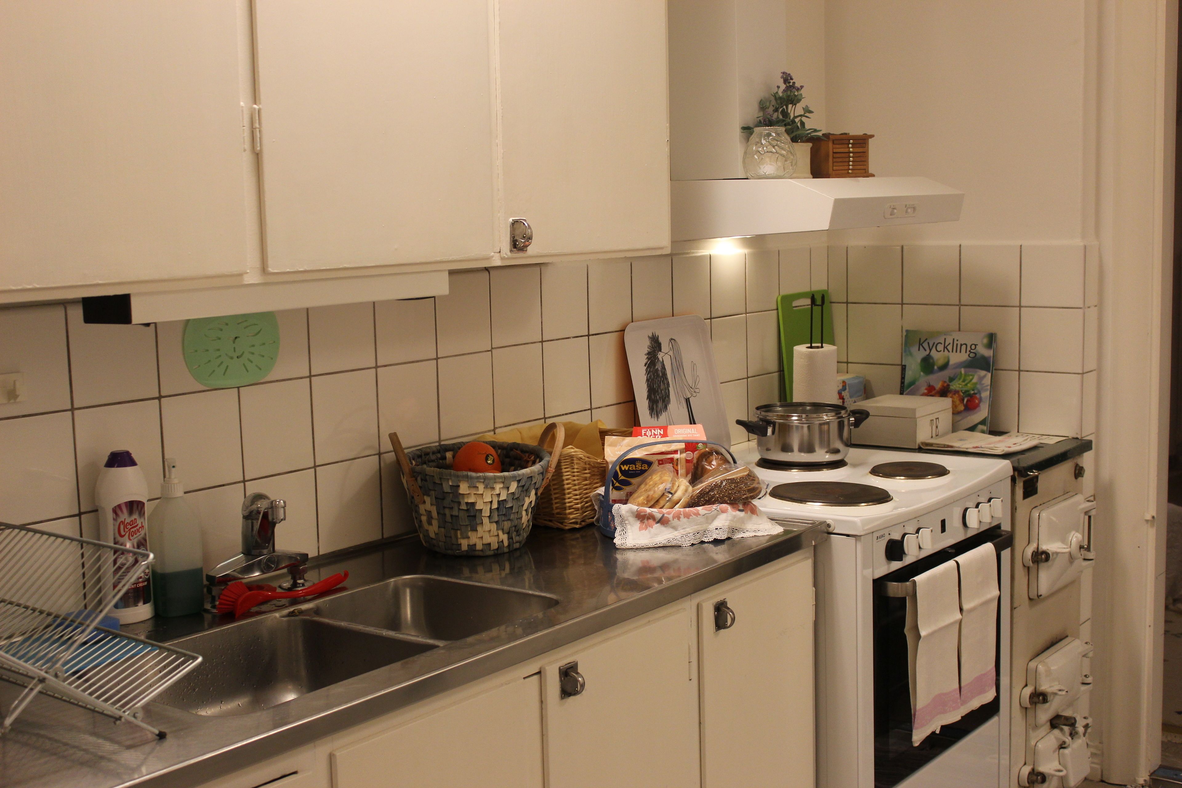 Una cocina con armarios blancos, un lavamanos de acero inoxidable, una estufa y varios utensilios de cocina sobre la encimera.