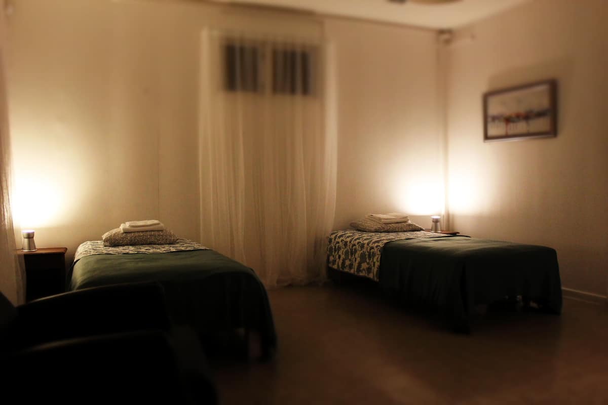 A dimly lit room with two single beds, a nightstand with a lamp, and a framed picture on the wall.