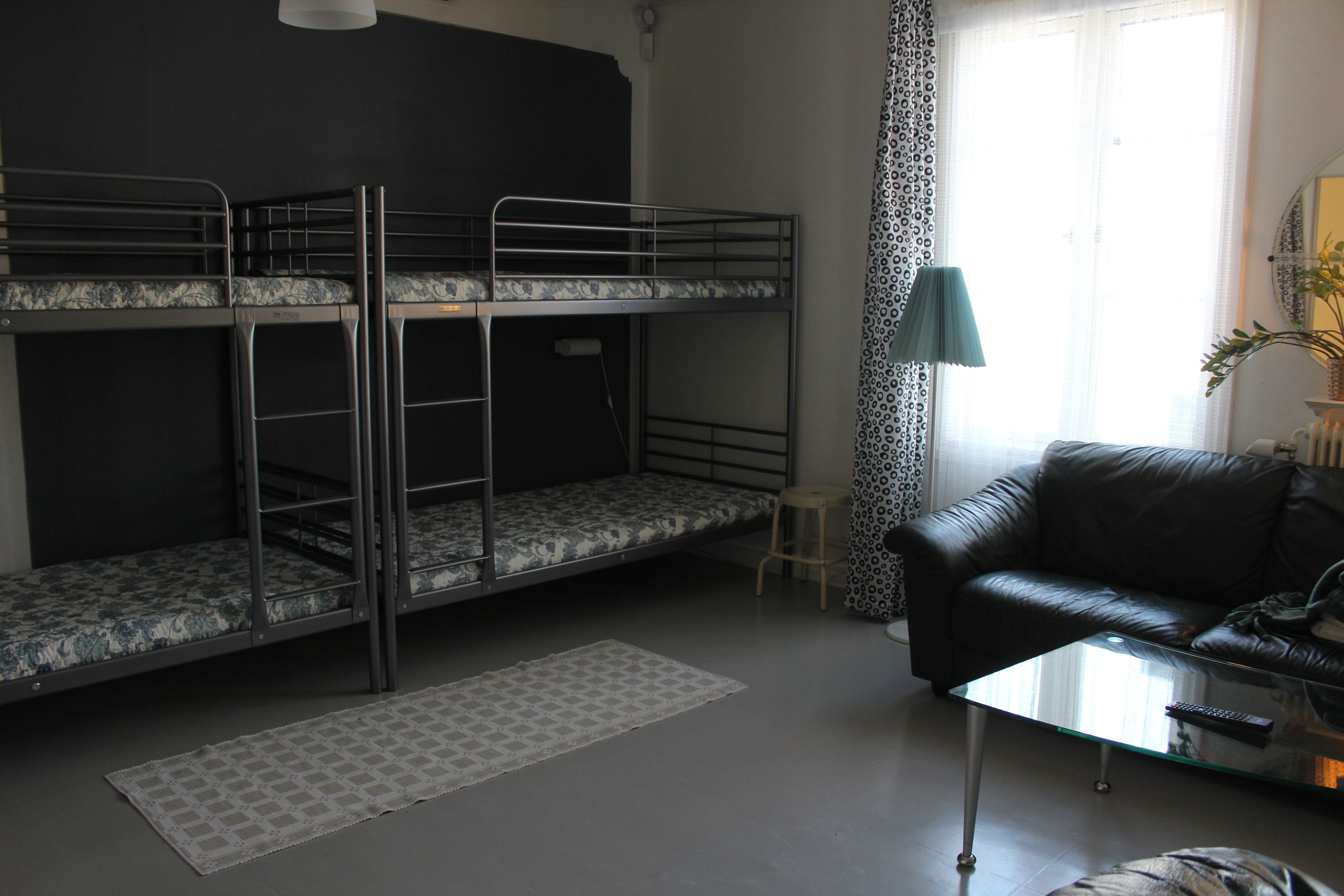 Una habitación con literas, un sofá de cuero, una mesita de cristal y un taburete pequeño.