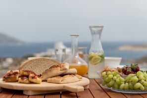Una mesa de madera con pan rebanado, una jarra de jugo, un vaso de agua con limón y un bol de uvas.