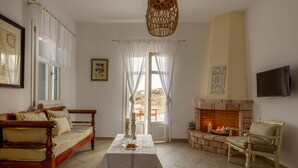 A cozy living room with a wooden sofa, a table with candles, a fireplace, and a television. - Kimolos Houses (Kimolos)