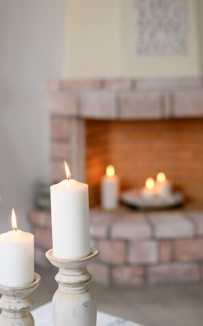 Dos velas blancas sobre candelabros frente a una chimenea.
