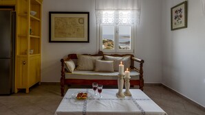 A cozy room with a wooden bench, a table with a candle, and a view of the sea through a window. - Kimolos Houses (Kimolos)