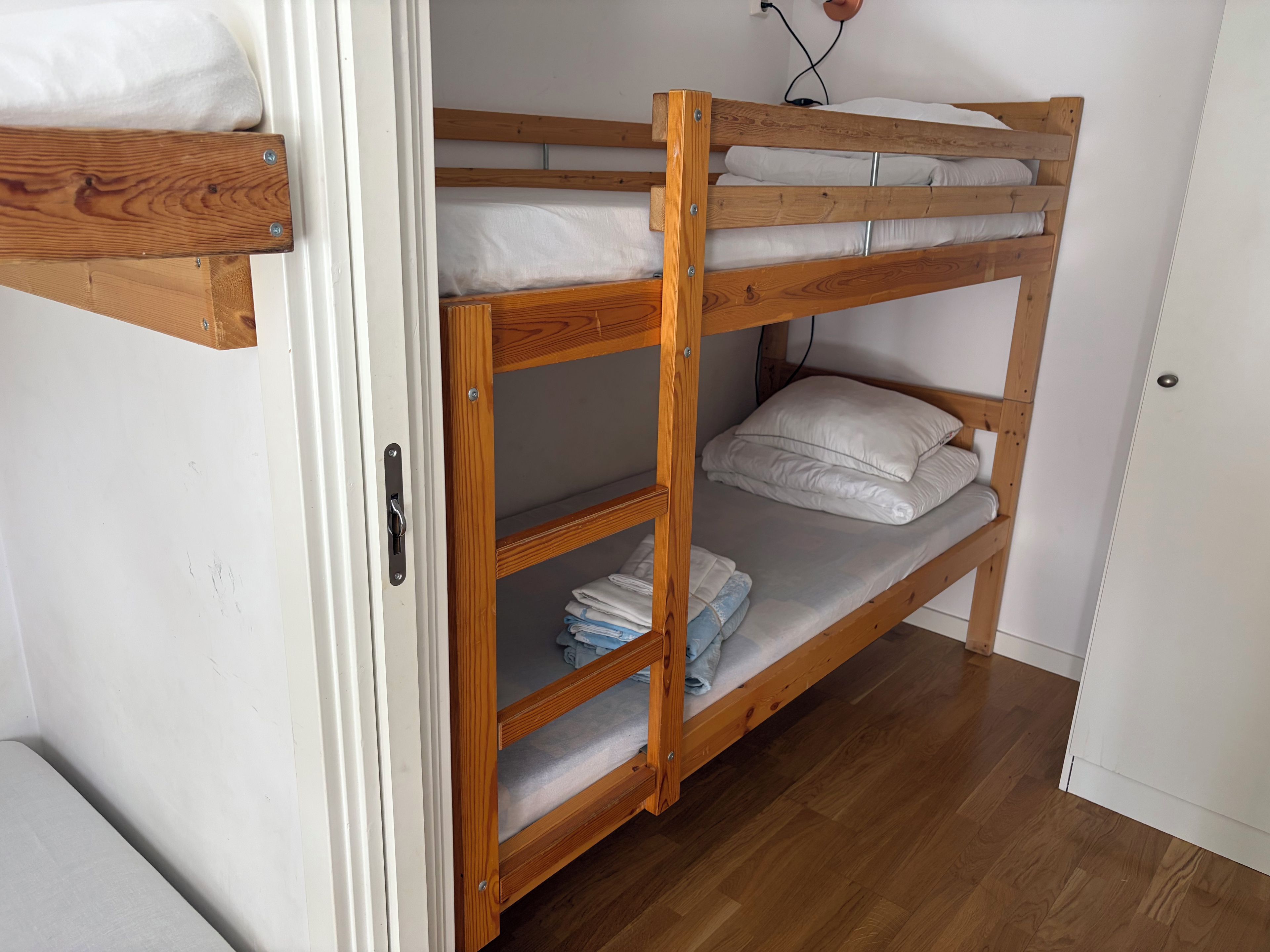 Un lit superposé avec une structure en bois, un matelas blanc et une étagère en métal.